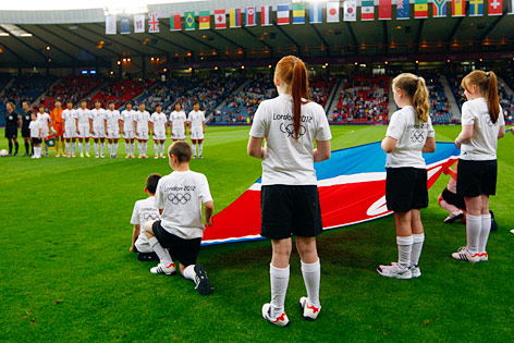 Spielerinnen Nordkoreas auf dem Feld, Kinder tragen die nordkoreanische Flagge